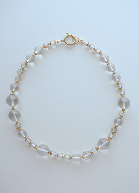 Beaded necklace with clear and gold accents on a light blue background